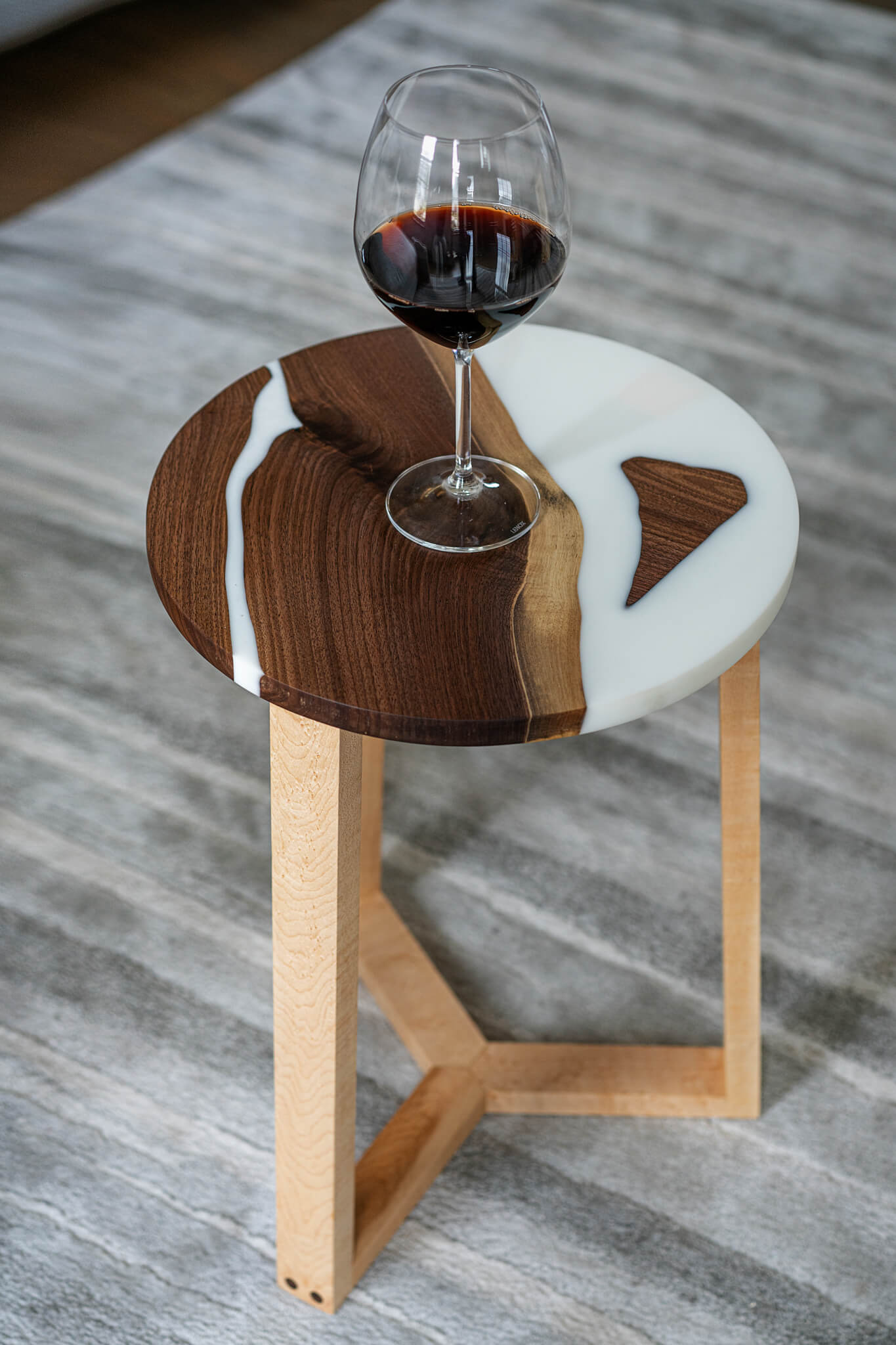 Image of a uniquely crafted round side table with a Walnut slab top, encased in white epoxy. The Maple legs add a striking contrast to the table, making it a perfect addition to any living space or office. The table showcases the beauty of natural wood grain, making each piece distinct and special.