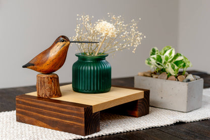 Photo depicts a Poplar plant stand, with stained legs and a hard-wax oil finish, perched on a wooden bridge. It cradles a decorative item, all while showing off the stunning wood grain detail.